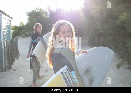 Portrait happy young female surfer with surfboard on sunny beach path Stock Photo