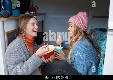 Happy young women friends eating instant noodles in camper van Stock Photo