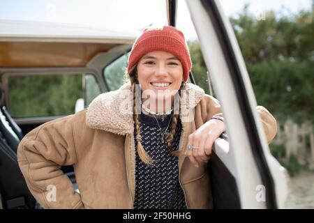 Portrait happy young woman in knit hat at camper van doorway Stock Photo