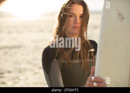 Portrait beautiful young female surfer in wet suit on sunny beach