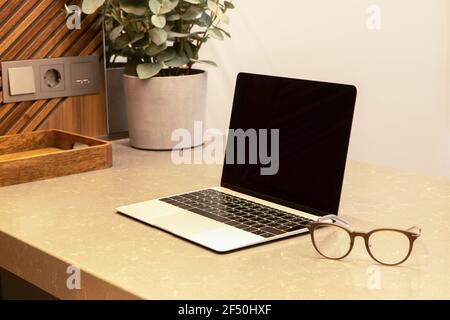 Workplace in apartment or cafe with modern interior. Open laptop and glasses on the table top. Business concept, remote work from home, distance learn Stock Photo