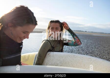 Happy young female surfers with surfboards on sunny beach Stock Photo