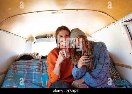 Portrait happy young women friends drinking tea in camper van Stock Photo