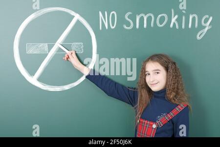Pre-adolescent girl points finger at drawn chalk crossed out cigarette and an inscription 'no smoking'. High resolution photo. Full depth of field. Co Stock Photo