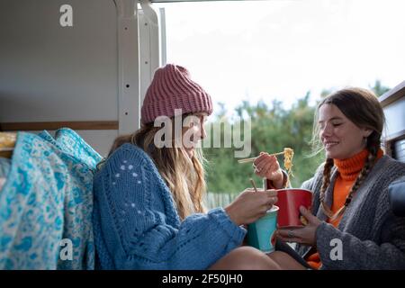 Young women friends eating instant noodles in camper van Stock Photo