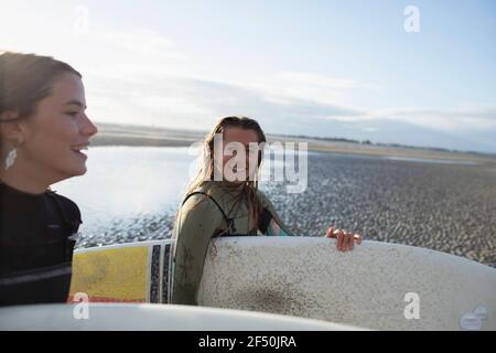 Happy young female surfers with surfboards on sunny beach Stock Photo