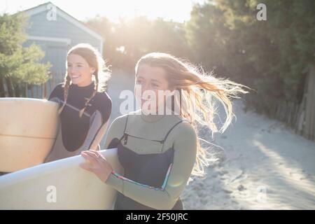 Happy young female surfers with surfboards on sunny beach path Stock Photo