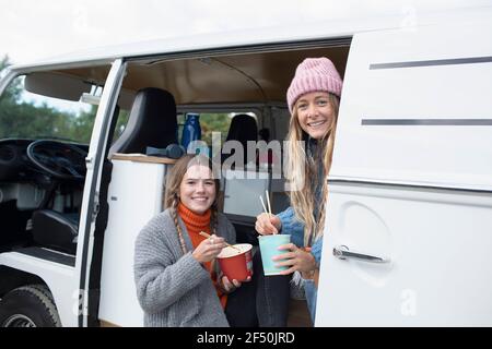 Portrait happy young women friends eating instant noodles in van Stock Photo