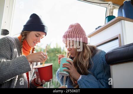 Young women friends eating instant noodles in camper van Stock Photo