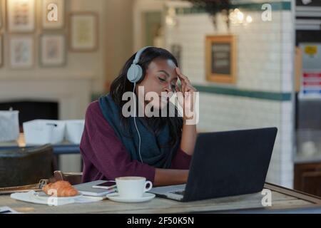 Tired young businesswoman with headphones working at laptop in cafe Stock Photo
