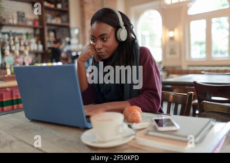 Young businesswoman with headphones working at laptop in cafe Stock Photo