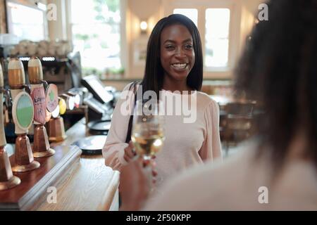 Happy young woman toasting wine glasses with friend in bar Stock Photo