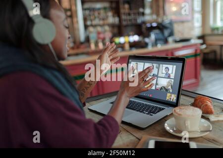 Woman video conferencing with colleagues at laptop on cafe table Stock Photo