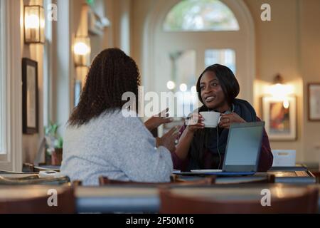 Businesswomen talking and drinking coffee at laptop in cafe Stock Photo