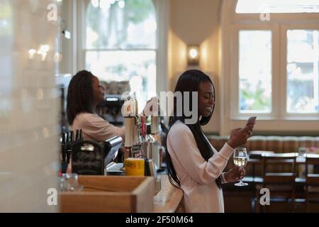 Young woman using smart phone and drinking wine in pub Stock Photo