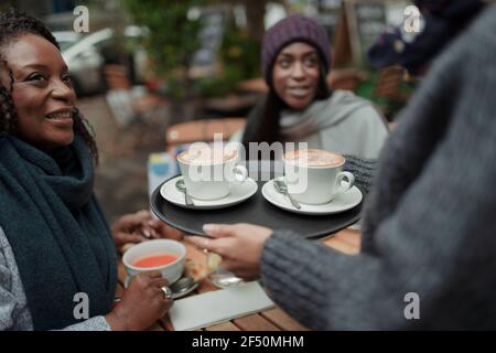 Waitress serving cappuccinos to mother and daughter at sidewalk cafe Stock Photo