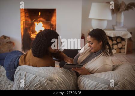 Mother and daughter using digital tablet on poufs at fireplace Stock Photo