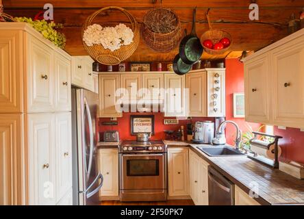 White painted oak wood cabinets and nuanced earth toned ceramic countertops in kitchen with pine wood floorboards, red painted walls inside old house Stock Photo