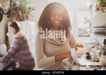 Portrait happy young woman drying dishes in sunny kitchen Stock Photo