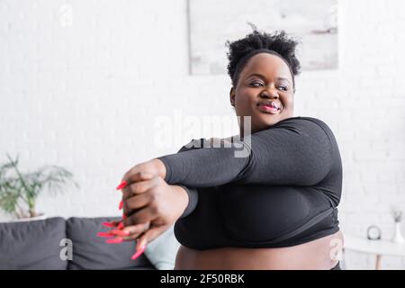 pleased african american overweight woman in sportswear exercising at home Stock Photo