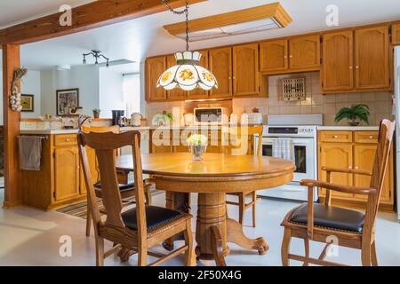 Red pine wood claw foot dining table with red oak wood and black leather seat high back chairs in kitchen with oak wood cabinets Stock Photo