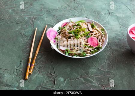 Soba noodles, tofu, and watermelon radishes in a bowl near chopsticks. Stock Photo