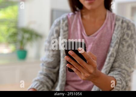 Caucasian woman sitting in kitchen using smartphone and smiling Stock Photo