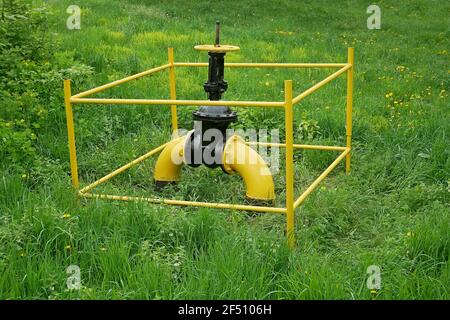 Large gas valve on the gas pipe outside among green grass and flowering plants in springtime Stock Photo