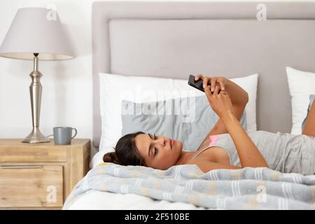 Caucasian woman lying on bed using smartphone and smiling Stock Photo
