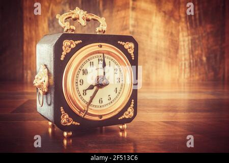 Old wooden alarm clock with gold applications, showing 8 o'clock on a wooden table Stock Photo
