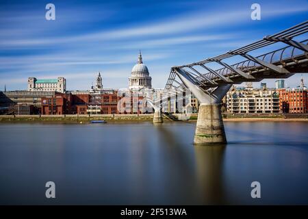 Millennium Bridge crossing the River Thames to St Paul's Cathedral in London, England. Long exposure with blurred clouds across a blue sky.