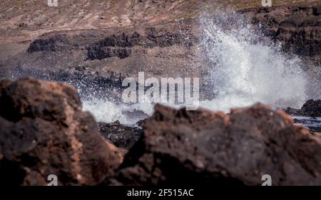 Big white waves clashing against the coast with black volcanic rocks in the foreground Stock Photo