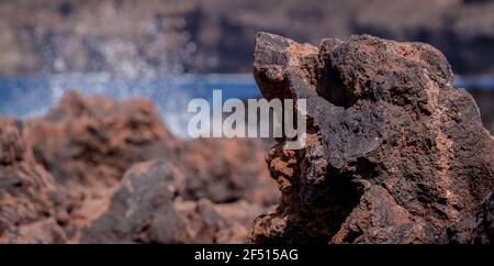 Detail of a dark volcanic rock on a sunny day with the sea in the background Stock Photo