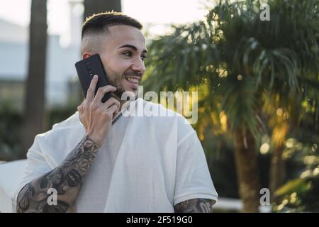 Handsome European man with tattooed arms talking on the phone and laughing Stock Photo