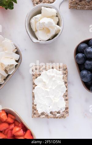 A healthy isolated cracker spread with cream cheese in the middle surrounded by trays full of fruit and a bowl with cream cheese over a marble board. Stock Photo