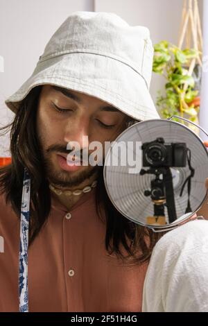 young long-haired photographer taking a self portrait at home with. young bohemian. wearing a pink shirt with a bucket hat. Stock Photo