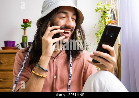 freelancer hipster man talking on two smart phones, young man multitasking, clothing stylist job, using a bucket hat. Stock Photo