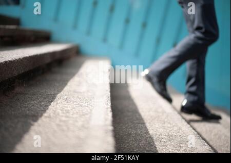 Business man in suit walking down stairs. Stepping down from higher position or white collar employee leaving / quitting job concept. London, UK Stock Photo