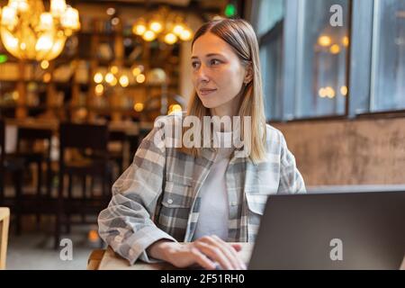 Young Caucasian business woman with blonde hair working on laptop in cafe. College student using technology , online education, freelance  Stock Photo