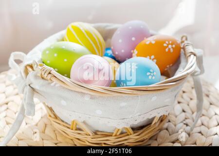 Easter colorful eggs in busket on white wooden table. Happy Easter background. Stock Photo