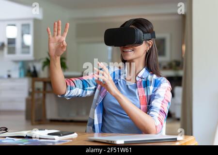 Caucasian woman sitting by desk using a vr headset and smiling Stock Photo