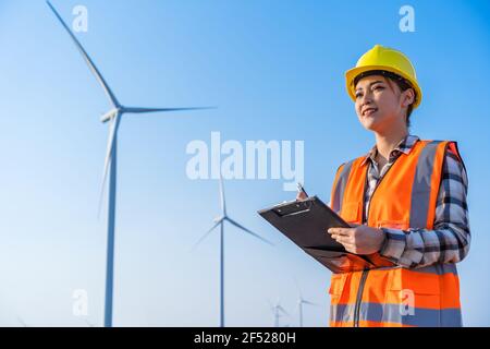 female engineer working and writing on a clipboard against wind turbine farm Stock Photo