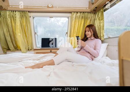 young woman using smartphone on bed of a camper RV van motorhome Stock Photo