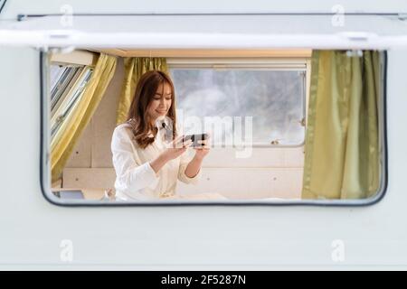 young woman using smartphone on bed of a camper RV van motorhome Stock Photo