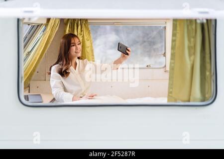 young woman selfie with smartphone on bed of a camper RV van motorhome Stock Photo