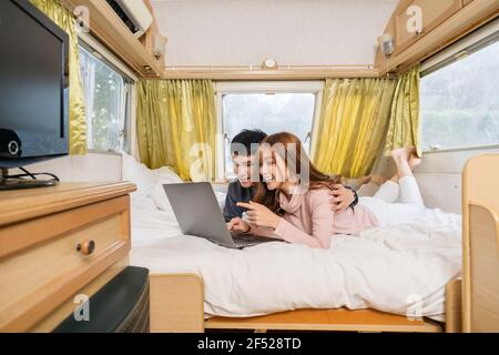 young couple using laptop computer on bed of a camper RV van motorhome Stock Photo