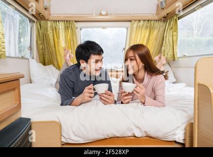happy young couple drinking coffee in bed of a camper RV van motorhome Stock Photo
