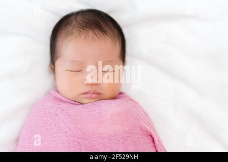 newborn baby sleep in pink cloth wrap blanket on a bed Stock Photo