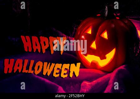 Halloween party and fall holidays concept with lit jack o'lantern pumpkin with scary glowing eyes and smile lighting the dark of night on velvet Stock Photo
