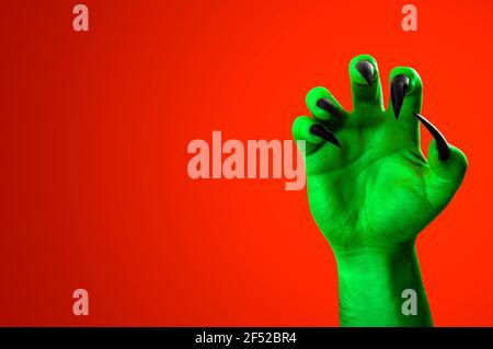 Halloween, nightmare creature and evil monster horror story concept with a scary zombie or demon hand with creepy long black nails isolated on orange Stock Photo